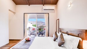 Una habitación de hotel con cama, mesita de noche, lámpara, ventana con cortinas y balcón con sillas y mesa.