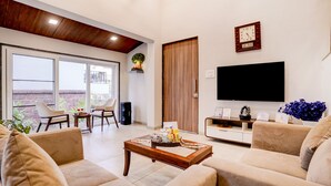 Una sala de estar con sofá, mesa de centro, televisor y vistas amplias a través de grandes ventanales.