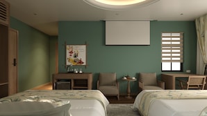 Ein Hotelzimmer mit zwei Betten, einem Schreibtisch, einem Stuhl, einem kleinen Tisch und einer Projektionsleinwand.