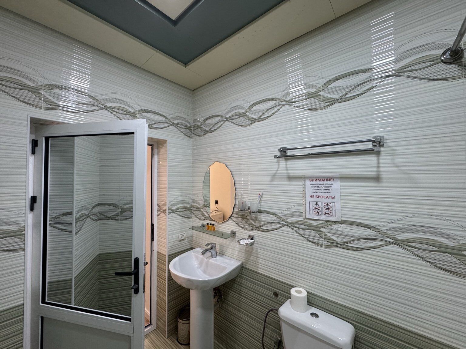 A bathroom with a glass door, a sink, a mirror, and a toilet.
