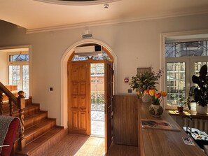 Escada de madeira que leva a um arco, uma mesa de recepção com um vaso de flores e uma vista pela janela.