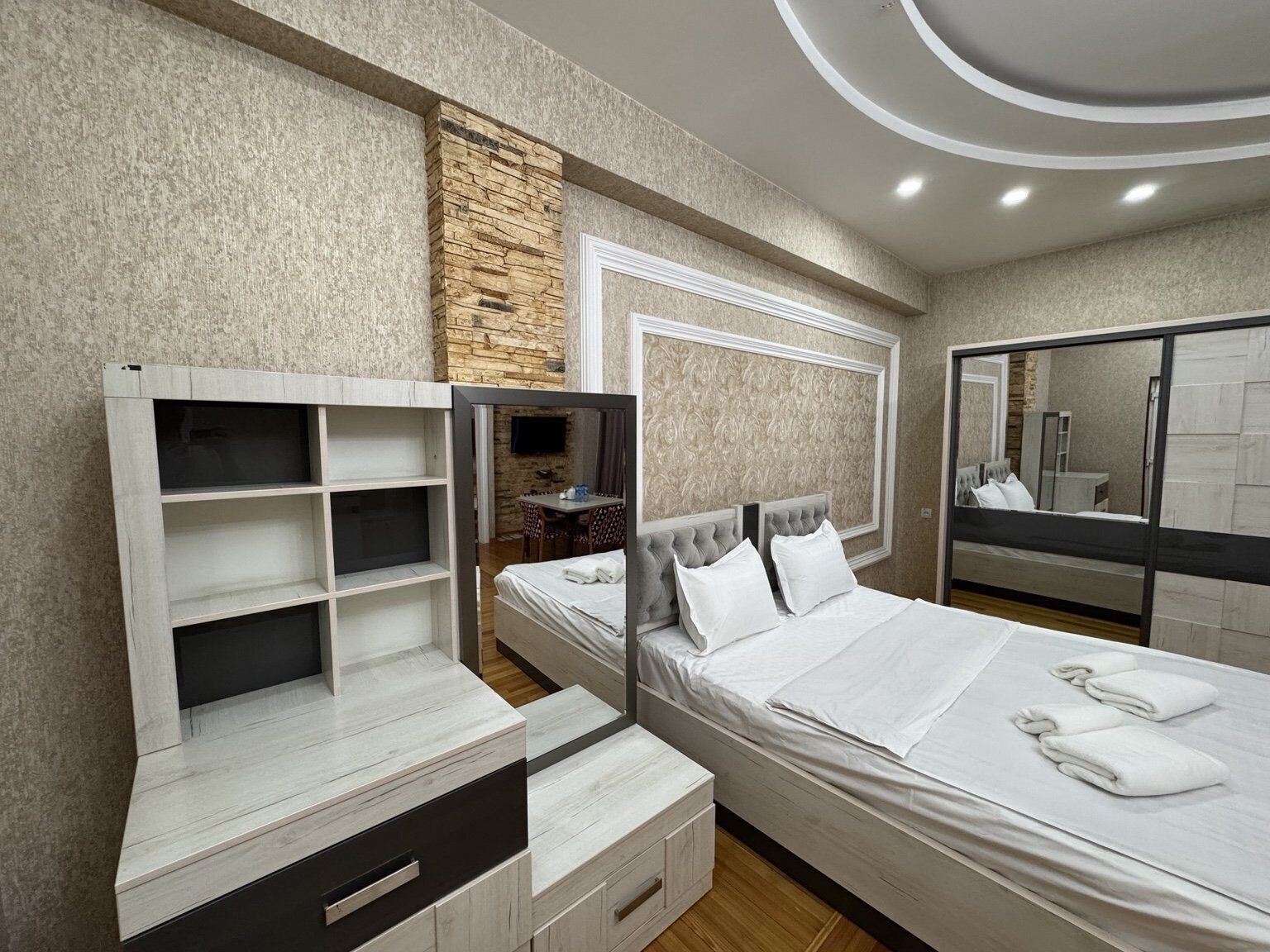 Een moderne slaapkamer met een bed, inbouwkasten, een spiegel en een accentmuur van steen.