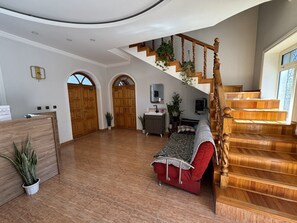 Uma sala de estar espaçosa com escada de madeira, um sofá vermelho e uma escrivaninha com computador.