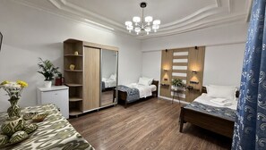 A hotel room with a wooden wardrobe, two beds, a desk with a plant, and a chandelier. - Giza Grand Hotel (Tashkent)