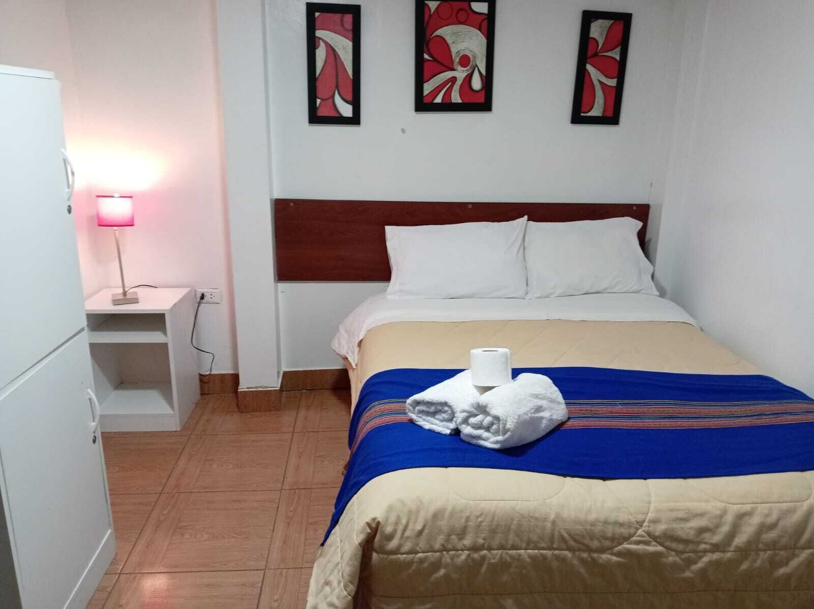 A hotel room with a bed, a nightstand with a lamp, and three wall art pieces.