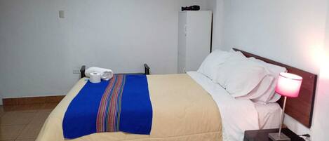 Una habitación de hotel con una cama, una lámpara de noche, un teléfono y un armario.