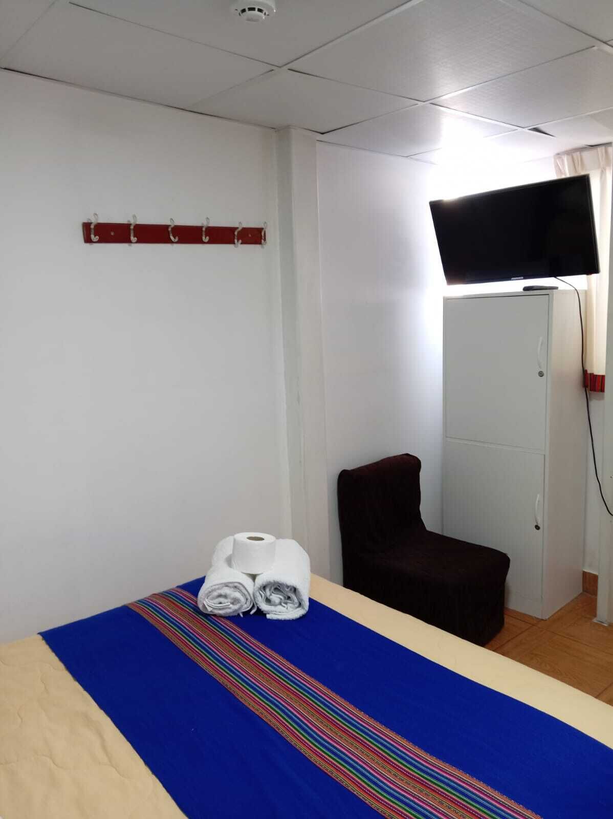A hotel room with a bed, a TV mounted on the wall, a wardrobe, and a small seating area.