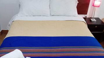 Una cama con almohadas blancas, una colcha azul y beige, una mesita de noche con lámpara y artículos de aseo.