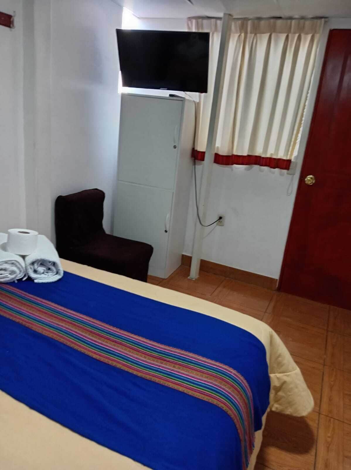 A hotel room with a bed, a TV mounted on the wall, a chair, and a door.