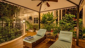 Un espacio al aire libre cubierto con dos sillones de descanso, un ventilador de techo y plantas en macetas.