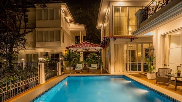 Una piscina con borde de baldosas, rodeada por un edificio blanco con ventanales grandes y un porche cubierto.