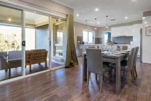 Eine moderne Küche mit weißen Schränken, ein Essbereich mit einem Holztisch und -stühlen sowie eine Glastür, die auf einen Balkon führt.