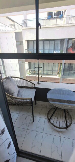 A balcony with a chair, a table, and a view of a building with balconies. - Beautiful 1-bedroom apt in Nairobi with fitness room, across street from Mall (Nairobi)