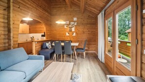 Interior de una cabaña de madera con sofá, mesa de comedor, sillas y zona de cocina.