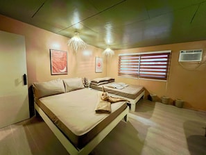 Un dormitorio con cama, mesitas de noche, una ventana con persianas y un aire acondicionado de pared.