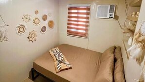 Une petite chambre avec un lit simple, un plafond en pente, une fenêtre avec des stores, des éléments de décoration murale et un appareil de climatisation.