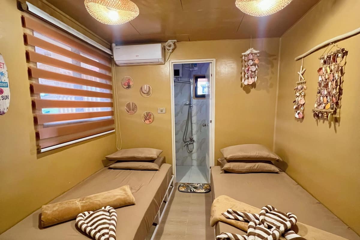 Una habitación con dos camas, ducha y un muro decorado con conchas marinas.