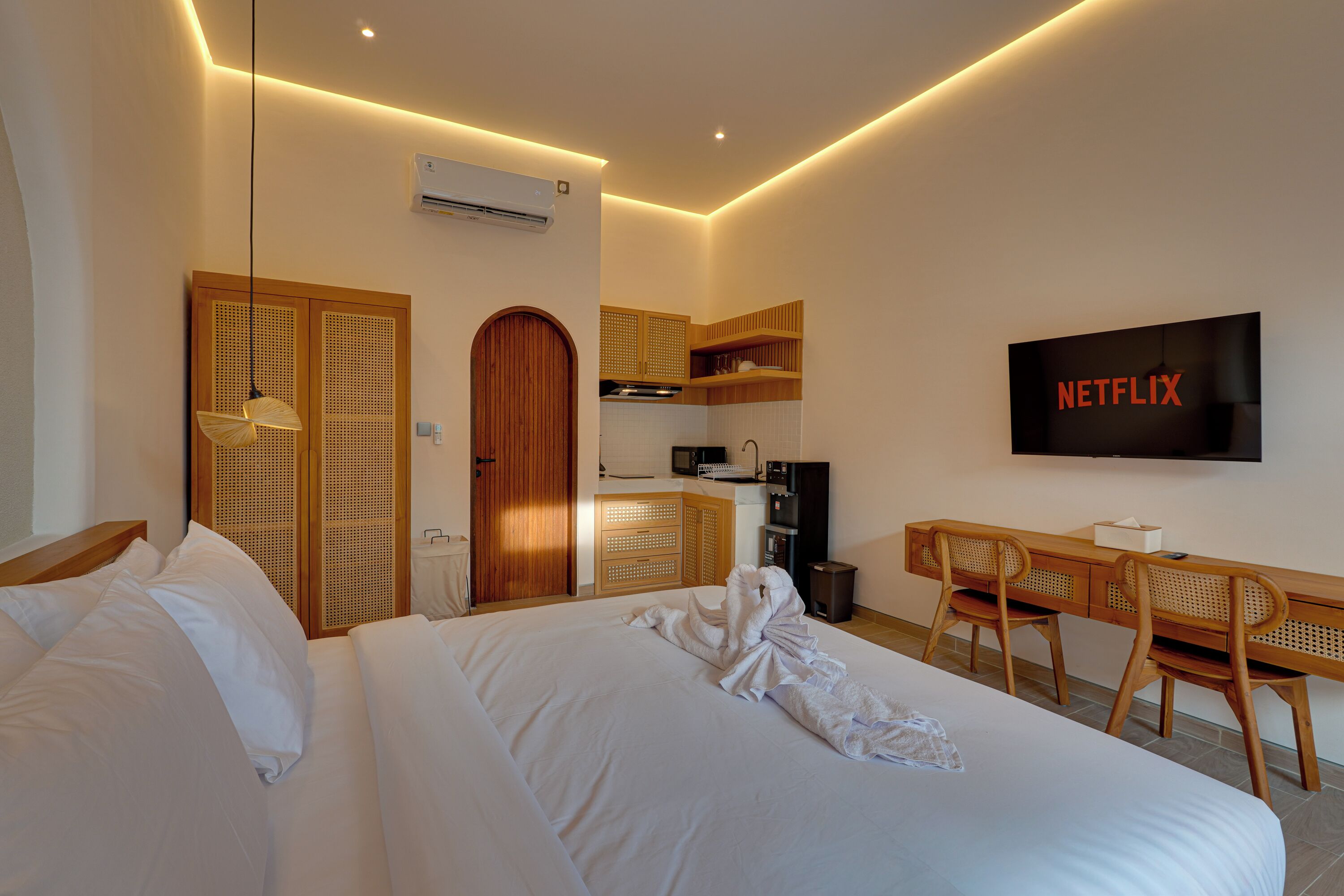 A hotel room with a bed, a desk with chairs, a TV, and a kitchenette.