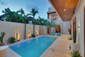 A swimming pool with a stone deck, surrounded by cacti and plants, with a wooden ceiling and a stone wall. - Loona Suites - Umalas (Kerobokan)