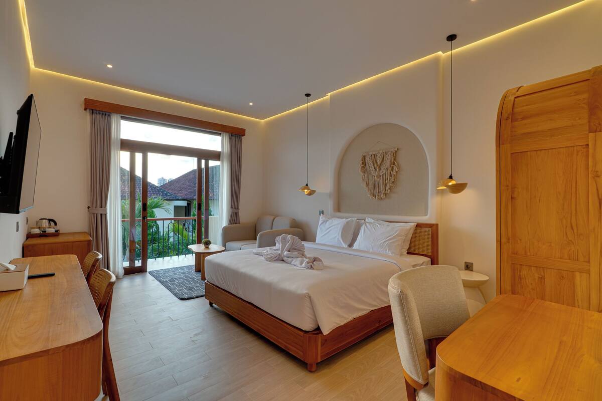 Ein modernes Hotelzimmer mit einem großen Bett, einem Schreibtisch, einem Stuhl, einem kleinen Tisch und einem Balkon mit Blick.