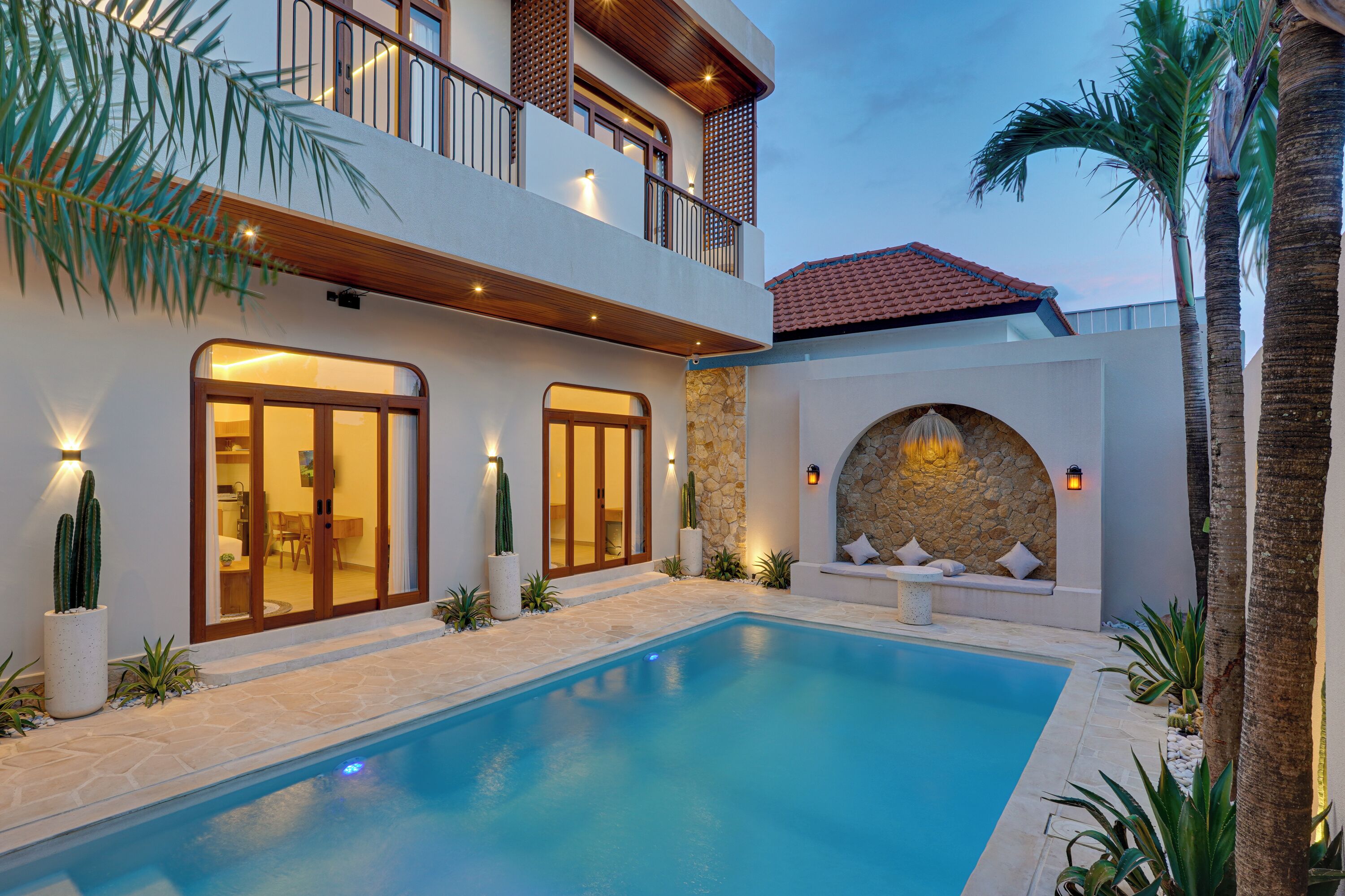 A modern two-story house with a swimming pool, stone walls, and a balcony with lighting.
