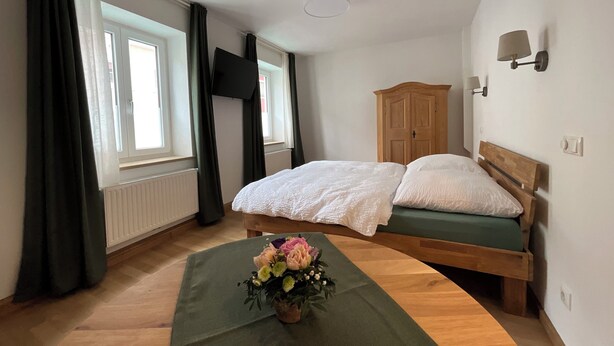 Ein Schlafzimmer mit einem Bett, einem Holzschrank, einem Fernseher und einem Fenster mit Vorhängen.