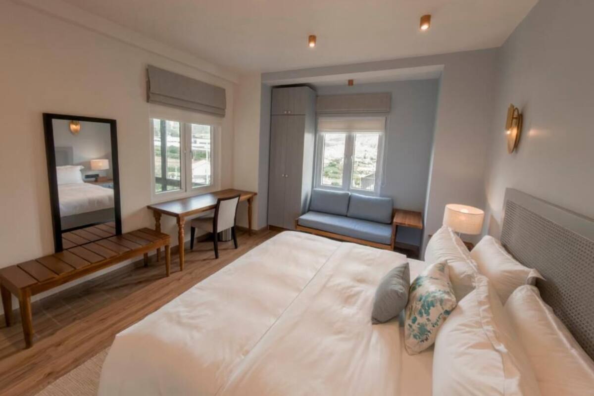 A bedroom with a large bed, a desk, a bench, a window, and a sofa.