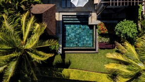 Ein Luftbild eines modernen Pools mit geometrischem Design, umgeben von üppiger Vegetation und Palmen.