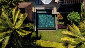 Vue aérienne d’une piscine moderne au design géométrique, entourée d’une végétation luxuriante et de palmiers.