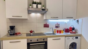 Een kleine keuken met een koffiezetapparaat, waterkoker, spoelbak en een wasmachine.