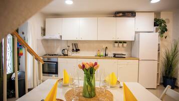 A modern kitchen with white cabinets, a stove, and a sink. There is a dining table with yellow placemats and a vase of flowers.