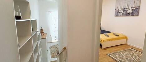 A bedroom with a bed, a painting, a rug, and a staircase leading to another room.