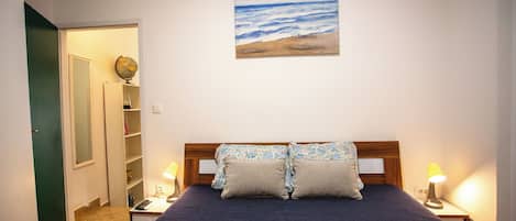 A bedroom with a bed, two bedside lamps, a painting of a beach, and a globe on a shelf.