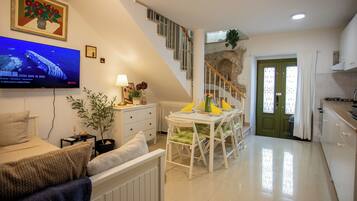 A modern living room with a flat-screen TV, a dining area with a table and chairs, a staircase, and a green door.