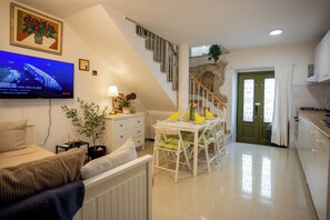 A modern living room with a flat-screen TV, a dining area with a table and chairs, a staircase, and a green door. - Casa Nora in Centre of Vodnjan (Vodnjan)