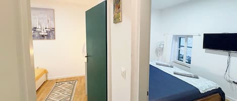 A bedroom with a bed, a window, a television, and a door leading to another room.