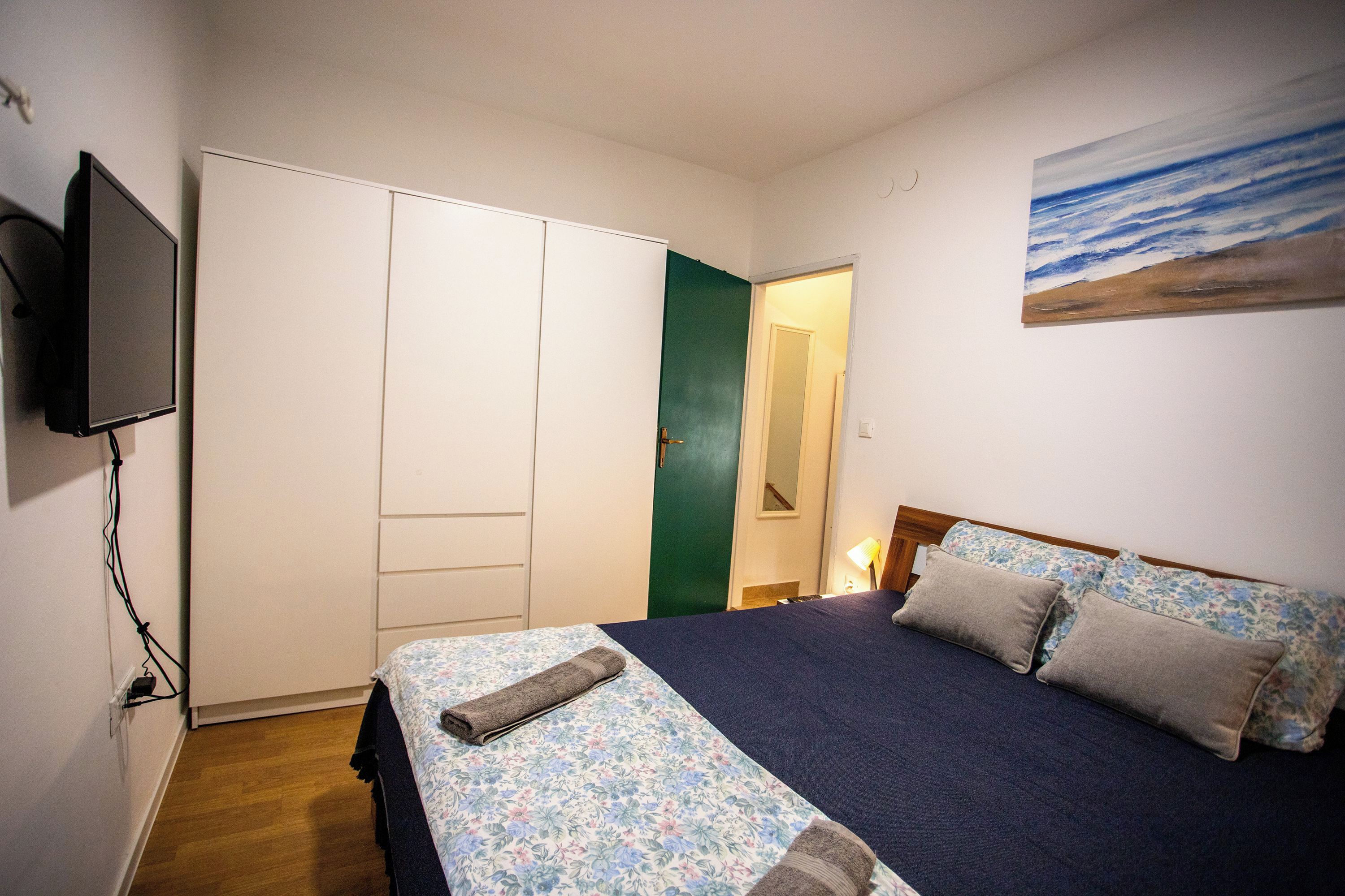 A bedroom with a bed, a television, a wardrobe, and a painting on the wall.