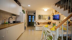 A modern kitchen with white cabinets, a dining area with a table and chairs, a staircase, and a living area with a sofa and a TV. - Casa Nora in Centre of Vodnjan (Vodnjan)