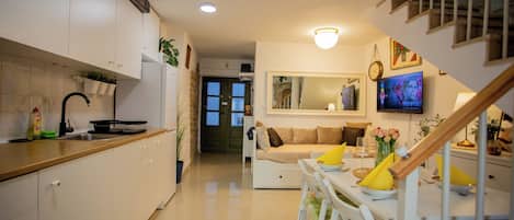 Una cocina moderna con armarios blancos, un comedor con mesa y sillas, una escalera y una sala de estar con sofá y televisor.