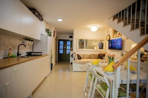 A modern kitchen with white cabinets, a dining area with a table and chairs, a staircase, and a living area with a sofa and a TV. - Casa Nora in Centre of Vodnjan (Vodnjan)