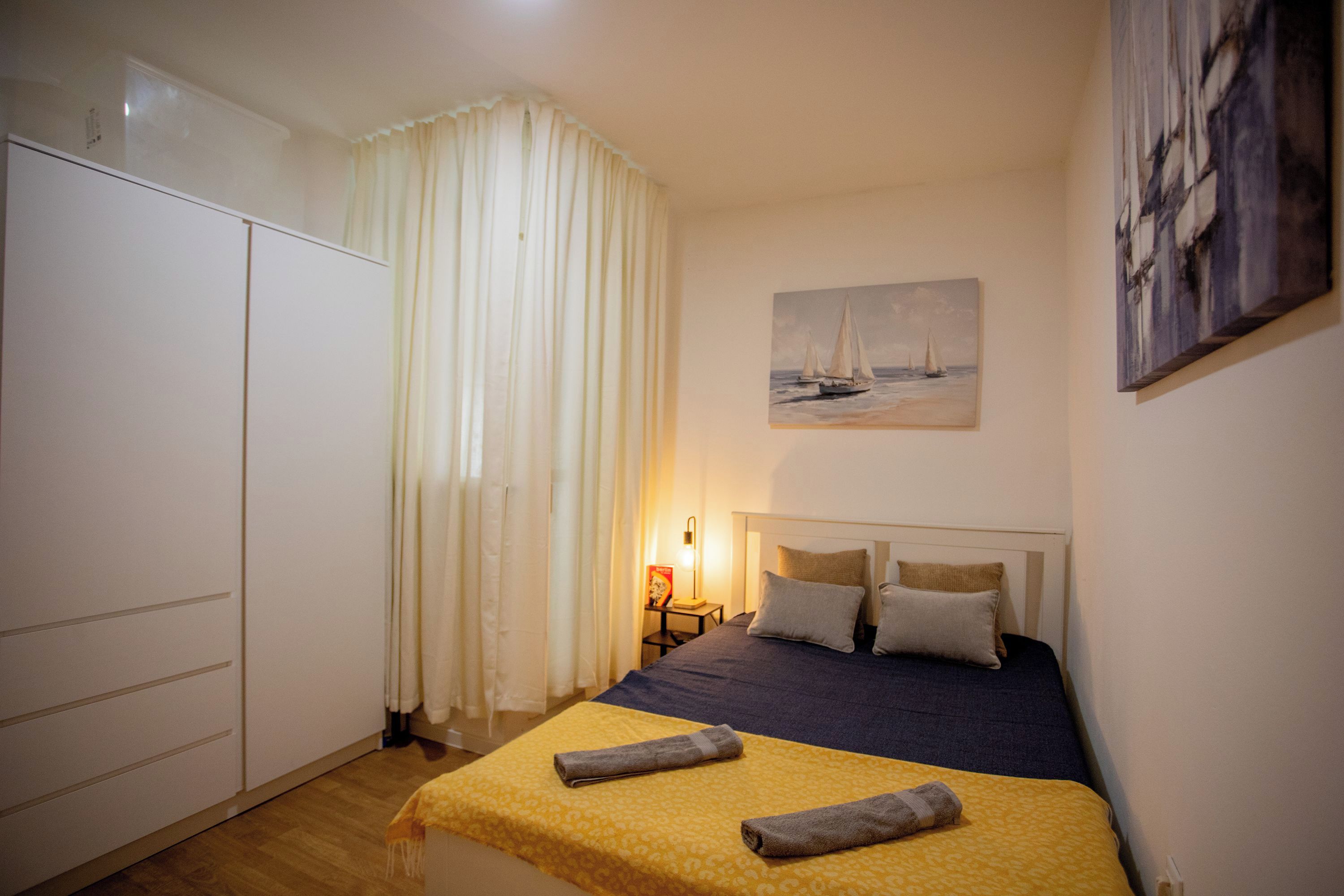 A bedroom with a bed, a nightstand, a painting, and a wardrobe.