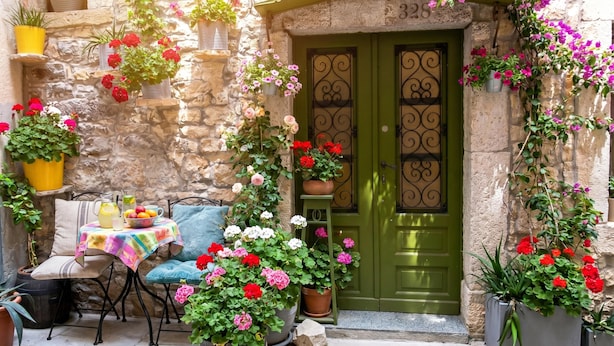A stone building with a green door, potted plants, a table with a colorful tablecloth, and outdoor seating. - Casa Nora in Centre of Vodnjan (Vodnjan)