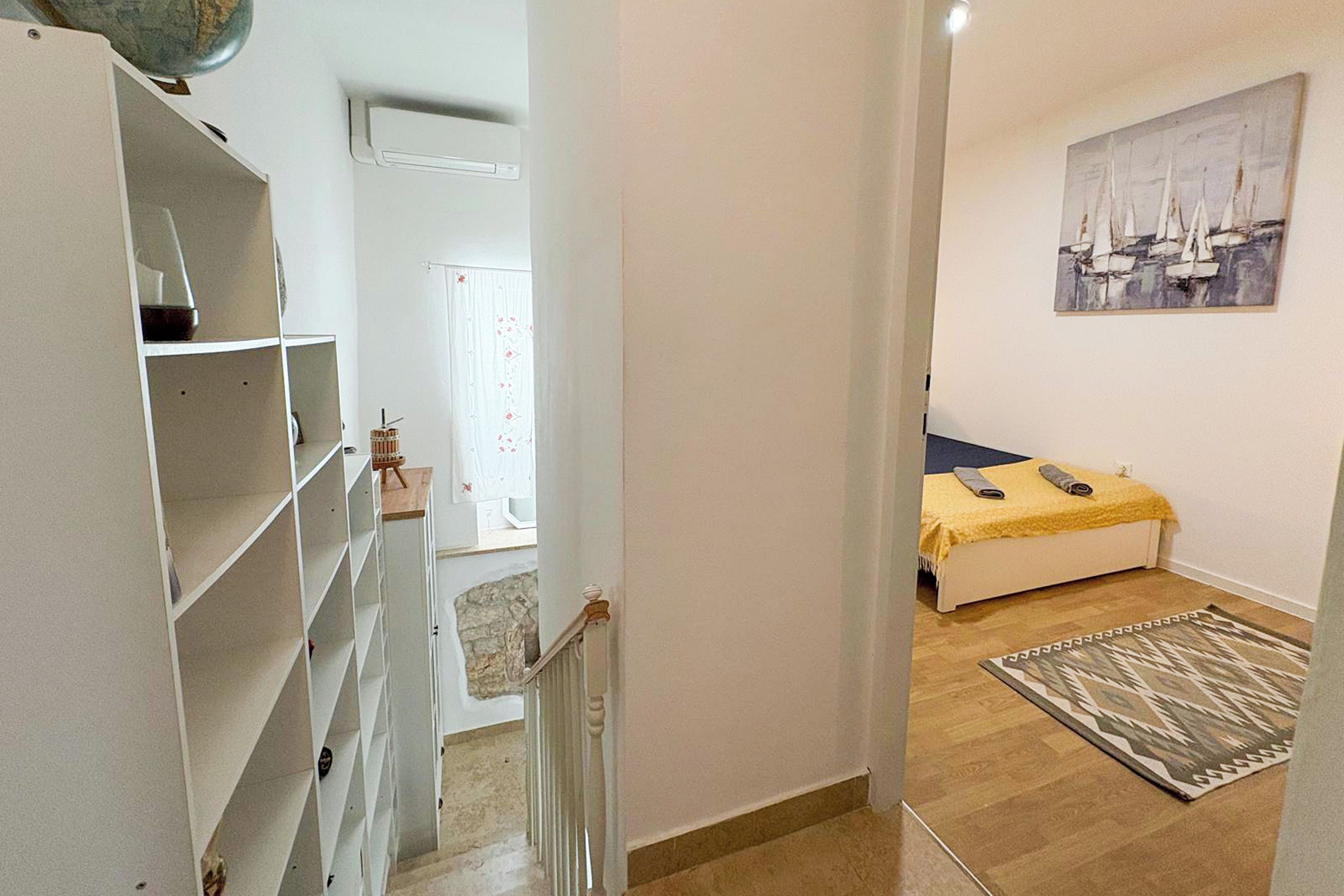 A bedroom with a bed, a painting, a rug, and a staircase leading to another room.