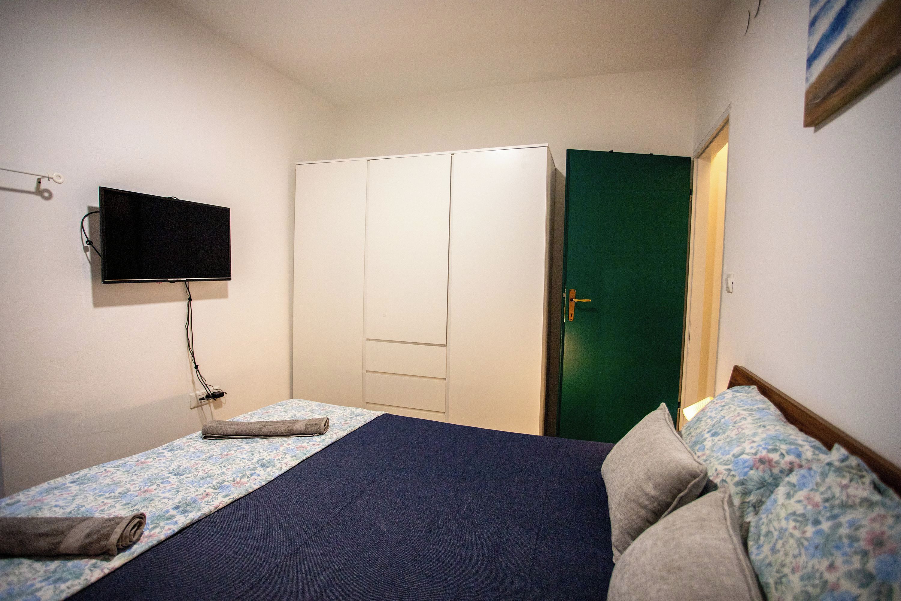 A bedroom with a bed, a wardrobe, a television, and a green door.
