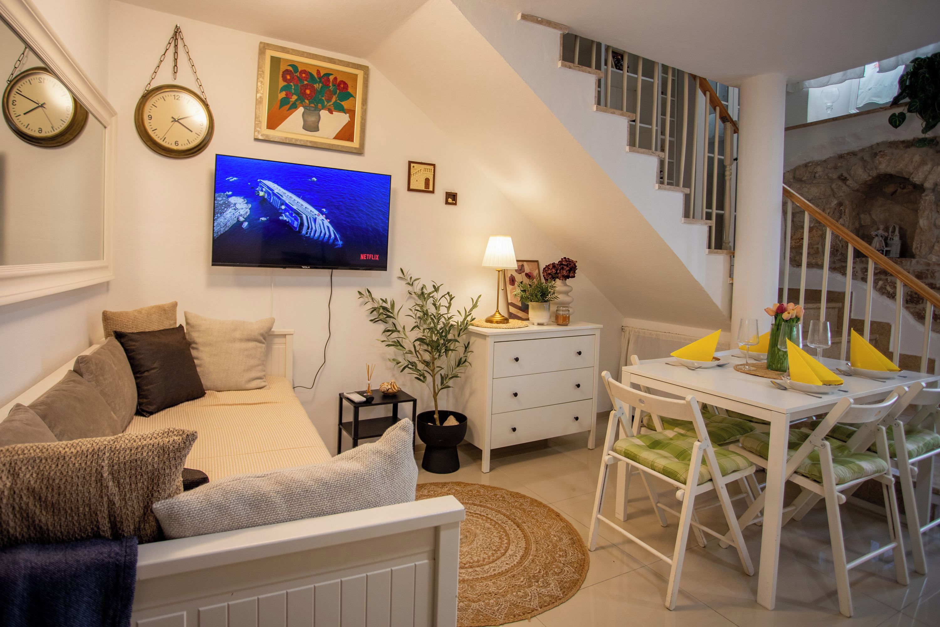 Een moderne woonkamer met een bank, een flatscreen-tv, een eettafel met stoelen en een trap.