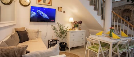 Een moderne woonkamer met een bank, een flatscreen-tv, een eettafel met stoelen en een trap.