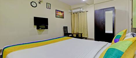A hotel room with a bed, a chair, a desk, a wall-mounted TV, a clock, and an air conditioning unit.