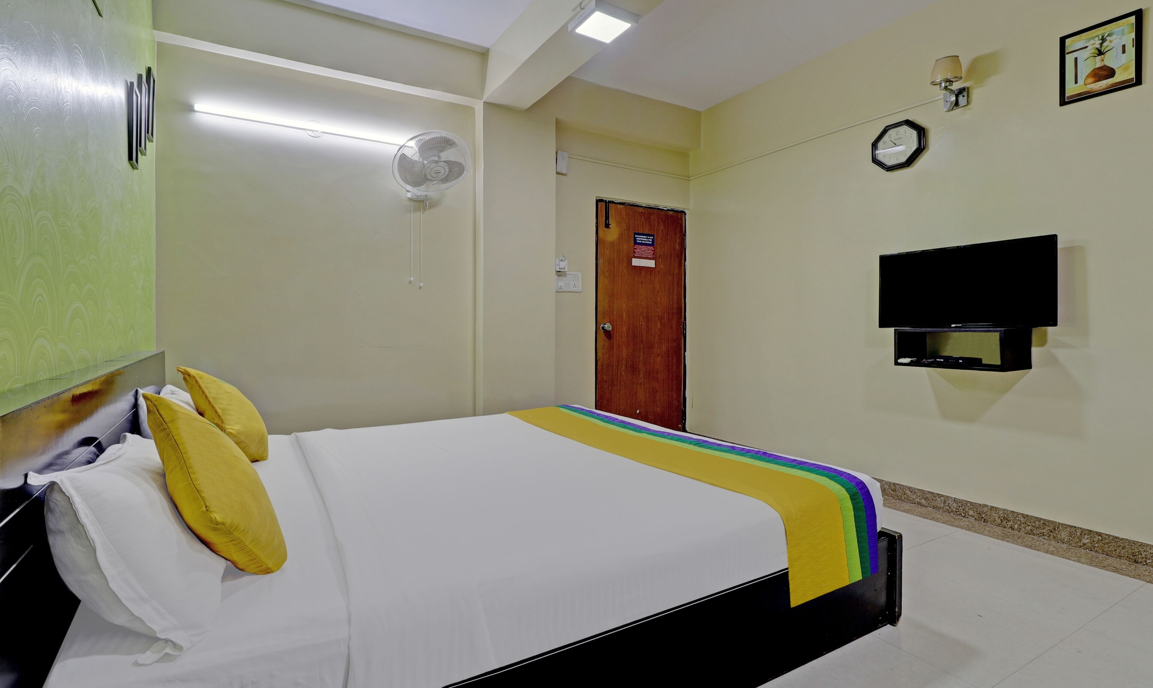 Ein Hotelzimmer mit Bett, Fernseher, einer Uhr und einer Tür.