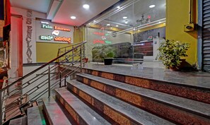 A hotel lobby with a staircase leading to the upper floor, a reception desk, and a large window with a view of the interior. - Palm Emirates, Koramangala (Bangalore)