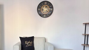 Een moderne woonkamer met een ronde salontafel, een bank, een decoratieve klok en een kussen met tekst.
